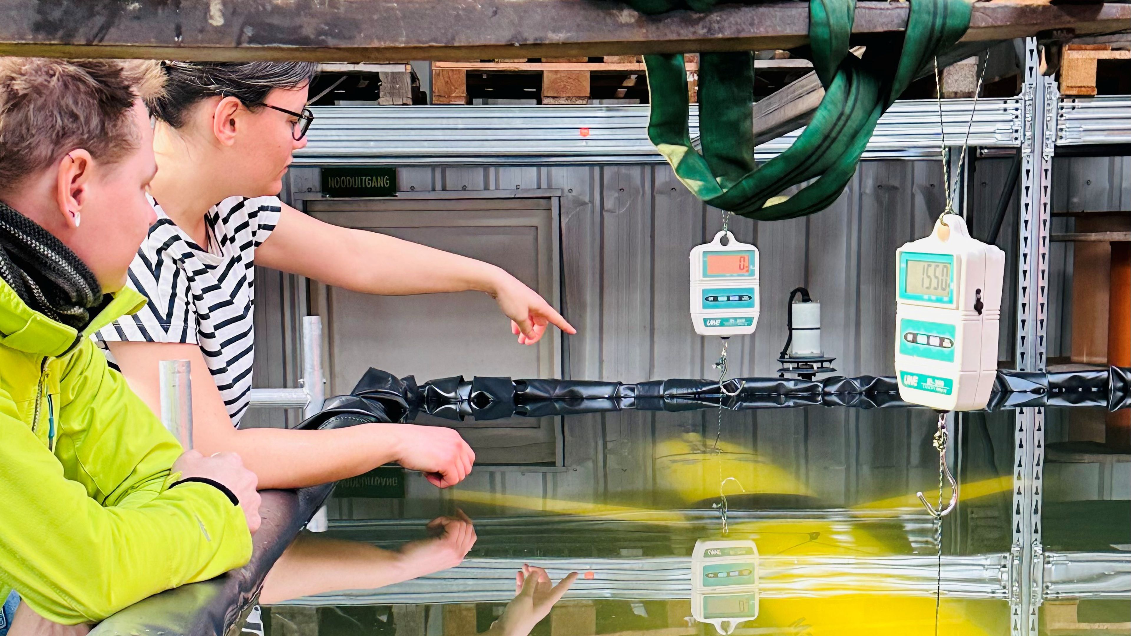 Photo of two persons looking into a bassin filled with water while testing glider ballasting