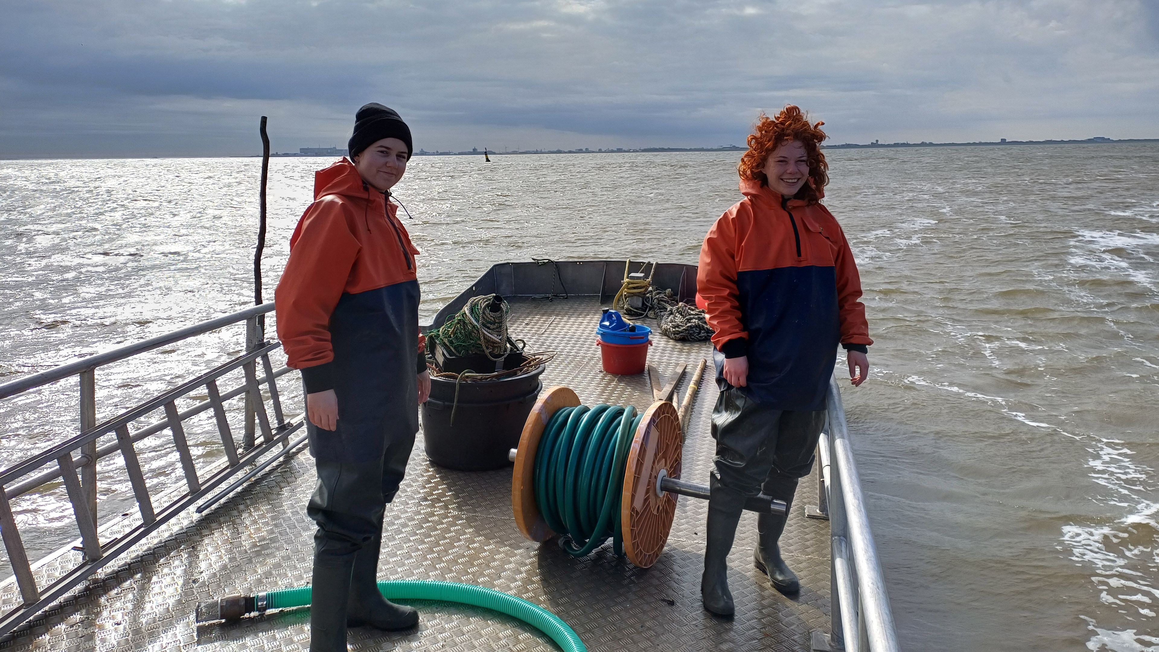 Photo of Rozemijn van Dam and Myrthe Bergsma standing on deck of a small boat on their way to build up the fykes in the Wadden Sea