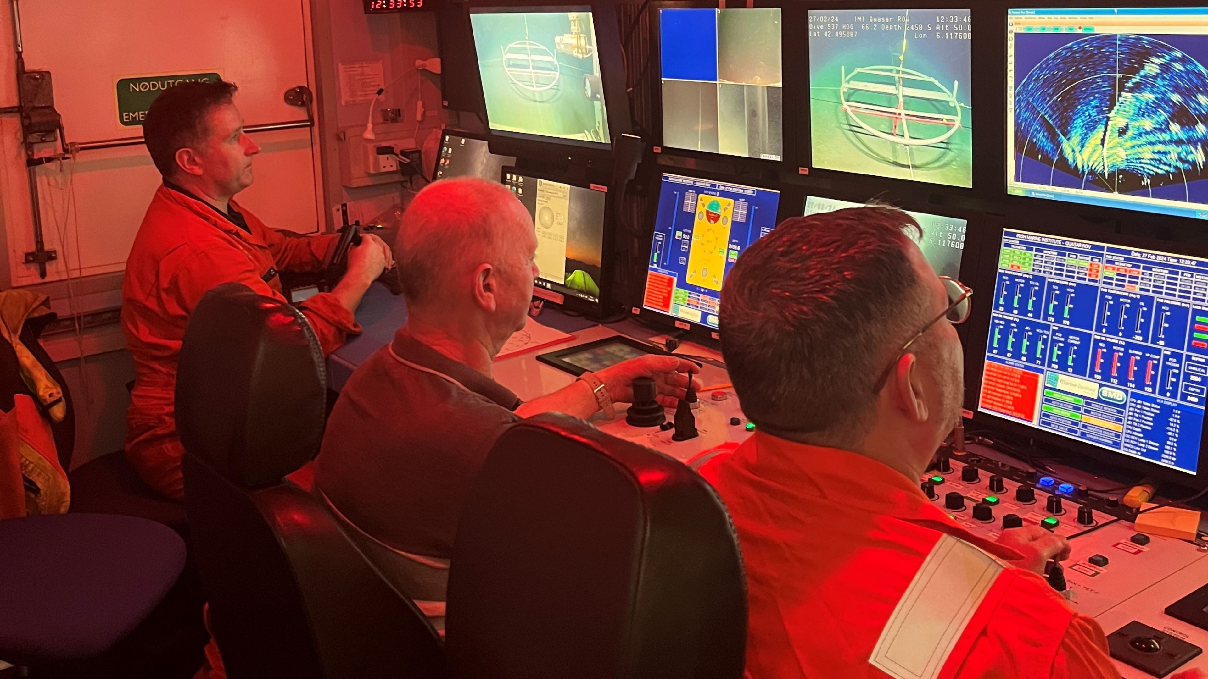 Three persons behing multiple screens in control room ROV