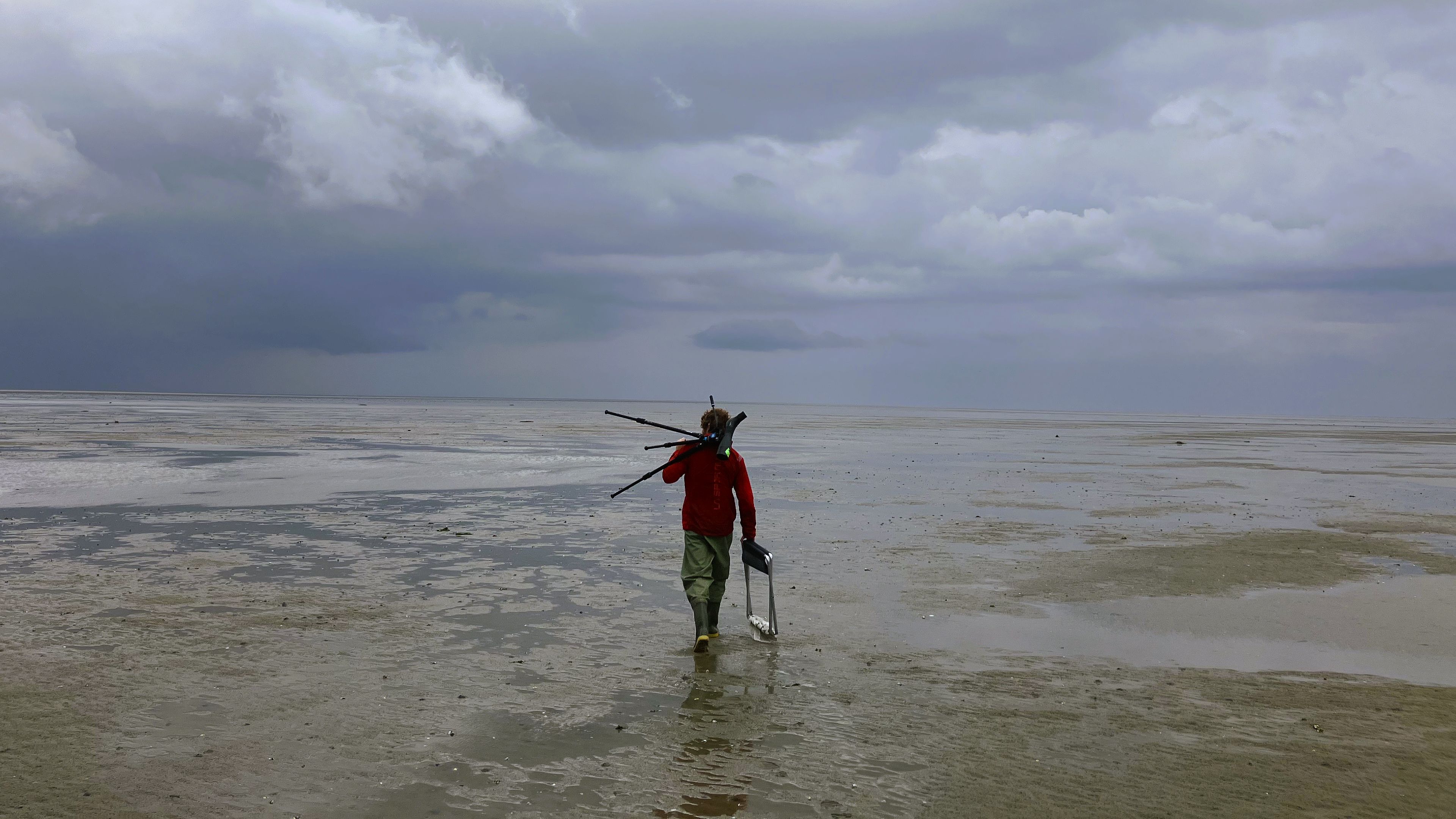 Photo of person walking in Wadden Sea with low tide and carrying equipment