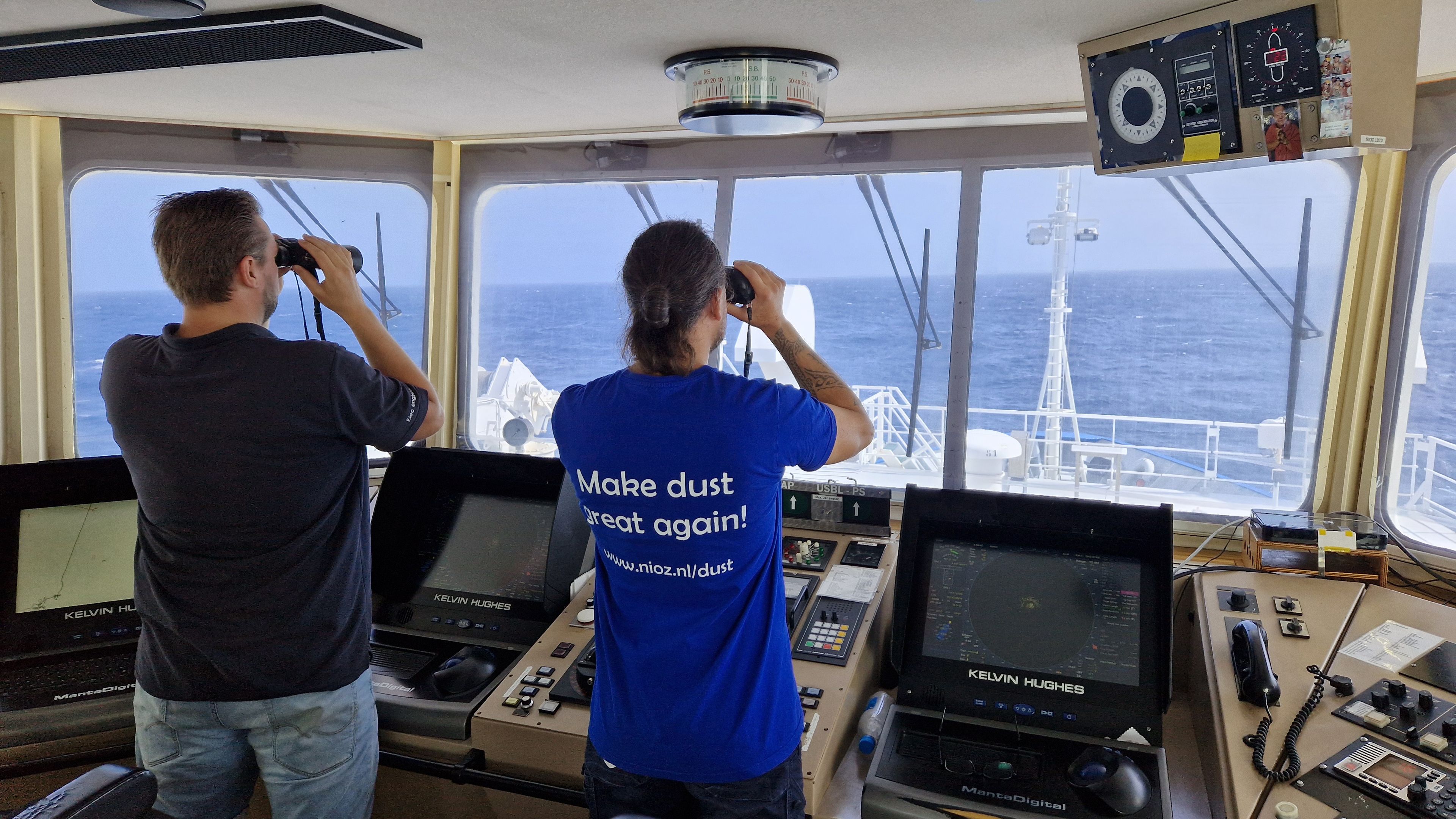 Two people in the control cabin of a research ship looking through binoculars
